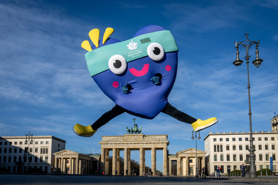 Maskottchen Unity springt freudig vor dem Brandenburger Tor in die Höhe