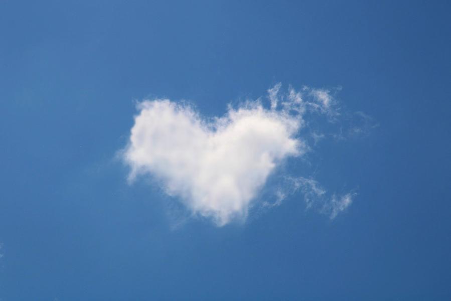 Eine herzförmige Wolke vor blauem Himmel.