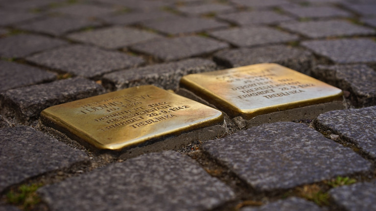 Das Foto zeigt zwei Stolpersteine, deren Inschrift unerkennbar ist, eingelassen in grauem Kopfsteinpflaster.