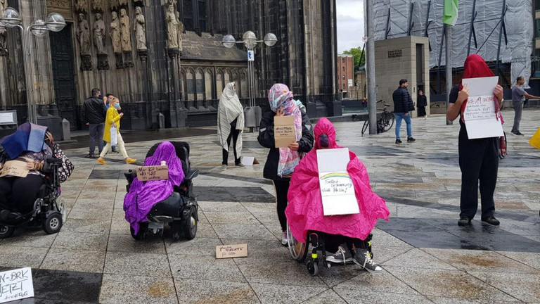 Stiller Protest mit Decken über dem Kopf und Protestschildern gegen das IPReG vor dem Kölner Dom.