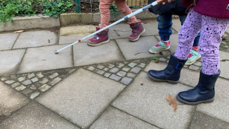 Drei Kinder, die einen Blindenstock benutzen