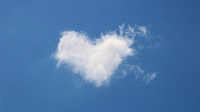 Eine herzförmige Wolke vor blauem Himmel.