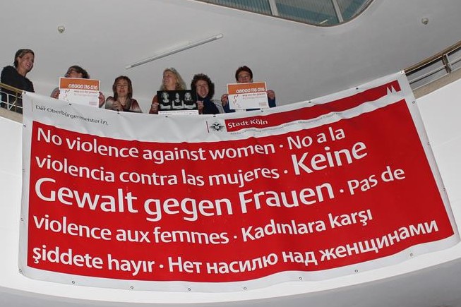 Das Bild zeigt Aktivistinnen auf einer Empore mit einem Bann "Keine Gewalt gegen Frauen" (in mehreren Sprachen).