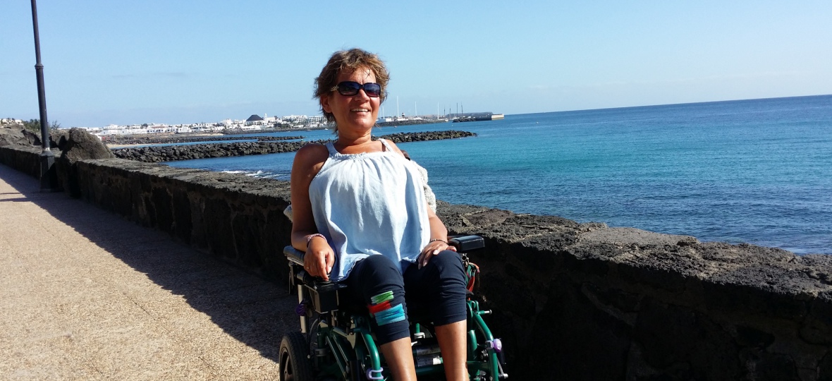 Corina Zolle steht in ihrem Rollstuhl sitzend vor einer Kaimauer. Ein Urlaubsfoto.
