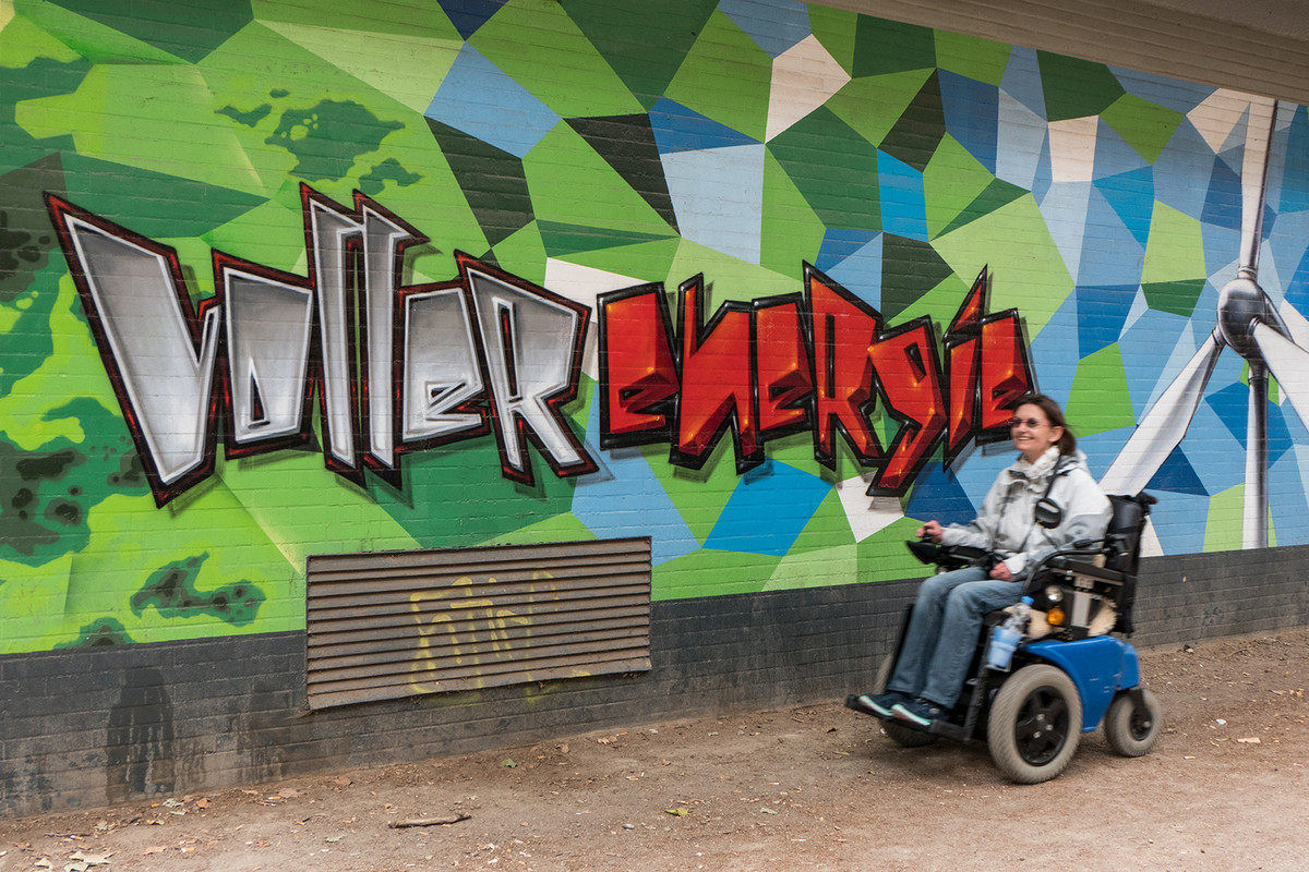 Silke Katzfuß fährt in ihrem E-Rolli an einem Graffiti vorbei: "Voller Energie"