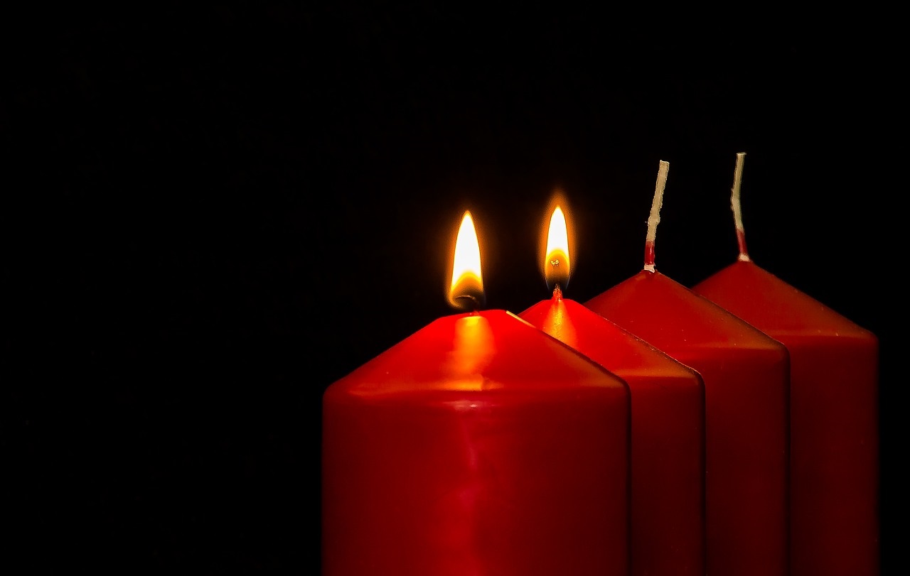Das Bild zeigt vier rote Kerzen, von denen zwei brennen.