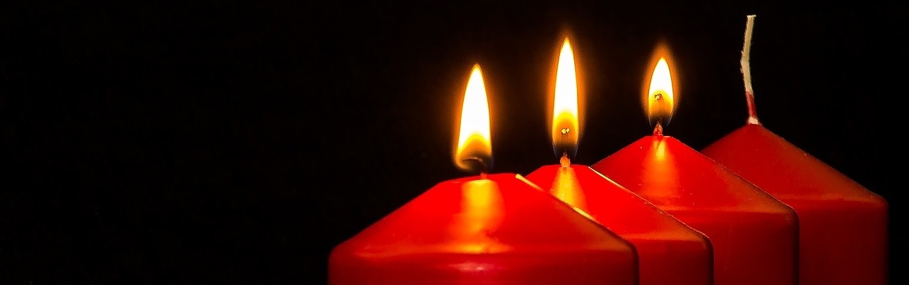 Das Bild zeigt vier rote Kerzen, von denen drei brennen.