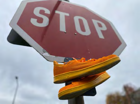 Orangenes Schuhpaar baumelt an dem Verkehrszeichen Stopp