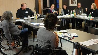 Eine gemischte Gruppe aus Menschen mit und ohne Körperbehinderung sitzt an einem Konferenztisch und diskutiert.