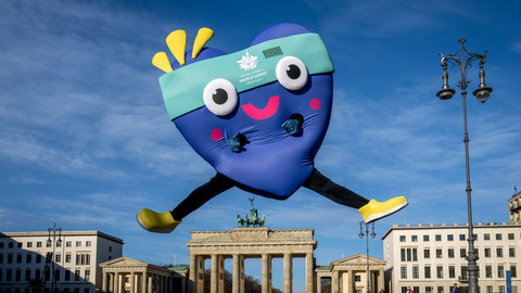 Maskottchen Unity springt freudig vor dem Brandenburger Tor in die Höhe
