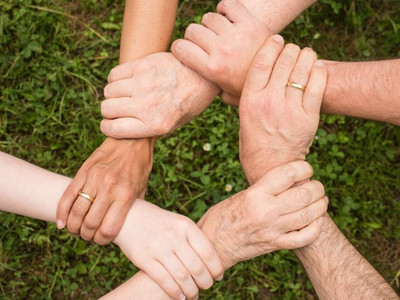 Mehrere Personen greifen mit nur einer Hand an das Handgelenk einer weiteren Person und stehen so, dass sie mit ihren Händen einen geschlossenen Kreis bilden.