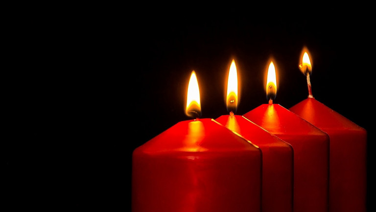 Das Bild zeigt vier rote Kerzen, die brennen.