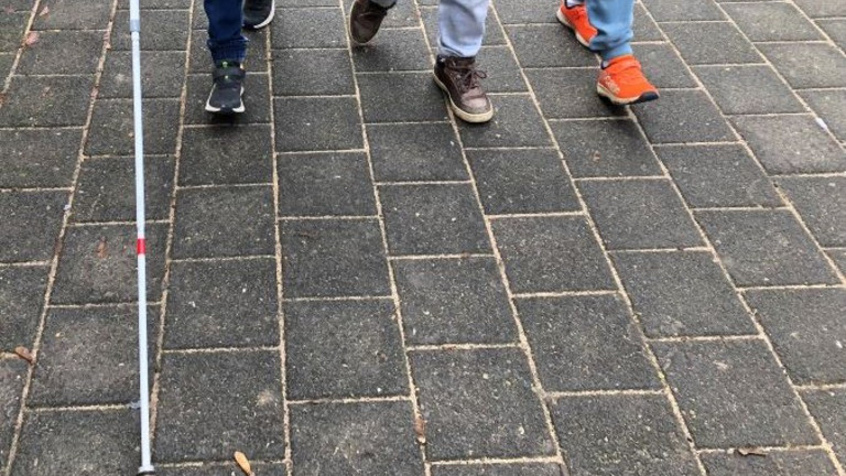 Füße von drei Kindern, die mit einem Langstock laufen