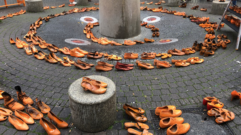Viele orangene Schuhe, zu ineinander liegenden Kreisen aufgestellt.