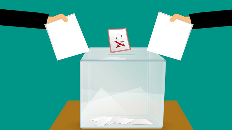 Zwei Stimmzettel werden in eine Wahl-Urne geworfen.