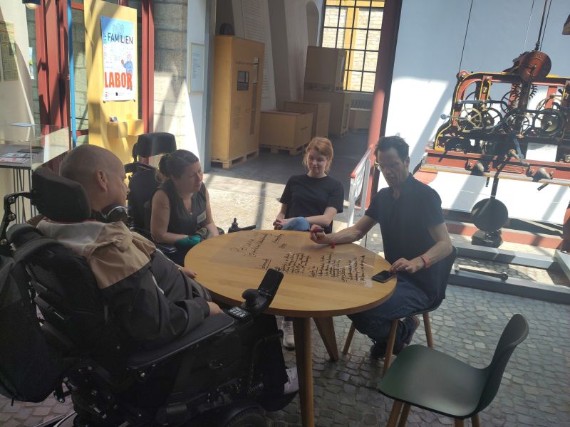 Zu sehen ist eine Arbeitsgruppe, die an einem rundenTisch sitzt und eine Folie gestaltet