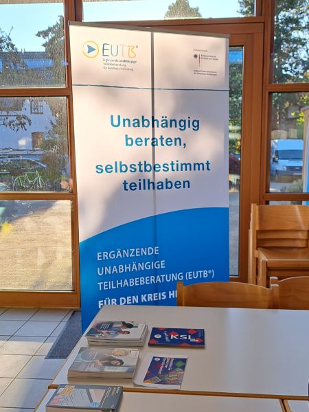 Auf einem Tisch liegen verschiedene Broschüren aus. Im Hintergrund steht ein Banner der EUTB (Ergänzende unabhängige Teilhabe-Beratung) mit der Aufschrift "Unabhängig beraten, selbstbestimmt teilhaben".