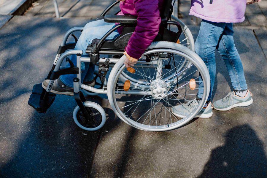 Zwei Mädchen probieren beim Sensibilisierungsworkshop die Rollstuhl-Station aus. Eine sitzt im Rollstuhl und versucht, eine Rampe hinauszufahren, während die andere ihr zur Seite steht und bereit ist, bei Bedarf zu unterstützen. Die Szene verdeutlicht anschaulich die physischen Herausforderungen und die Bedeutung von Hilfsbereitschaft im Alltag.