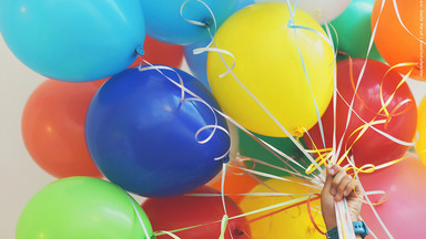 Eine Hand hält viele bunte Luftballons.