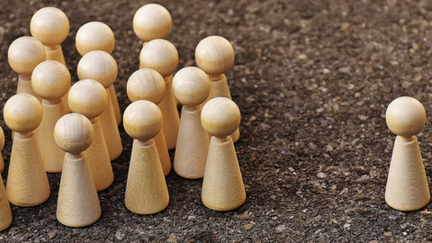 Eine einzelne Holzfigur steht mit Abstand neben einer Gruppe Holzfiguren.
