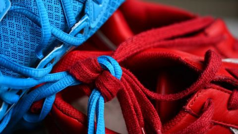 Ein Sportschuh in blau und ein Sportschuh in rot sind an den Schnürsenkeln zusammengeknotet.