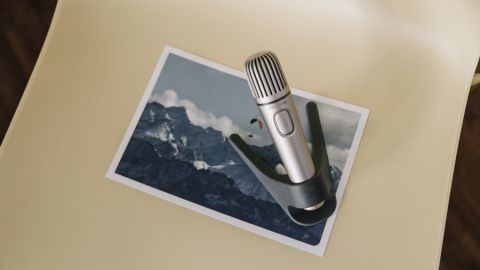 Nahaufnahme eines Mikrofons im Vordergrund. Im Hintergrund ist ein Foto mit Bergen unter blauem Himmel zu sehen.
