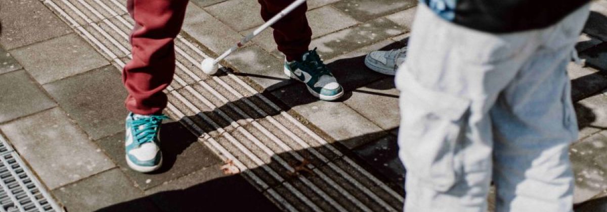Zwei Jungen erkunden das Blindenleitsystem der Schule mit dem Langstock und erfahren so direkt, wie Menschen mit Sehbehinderungen Wege finden und welche Hindernisse im Alltag lauern können.