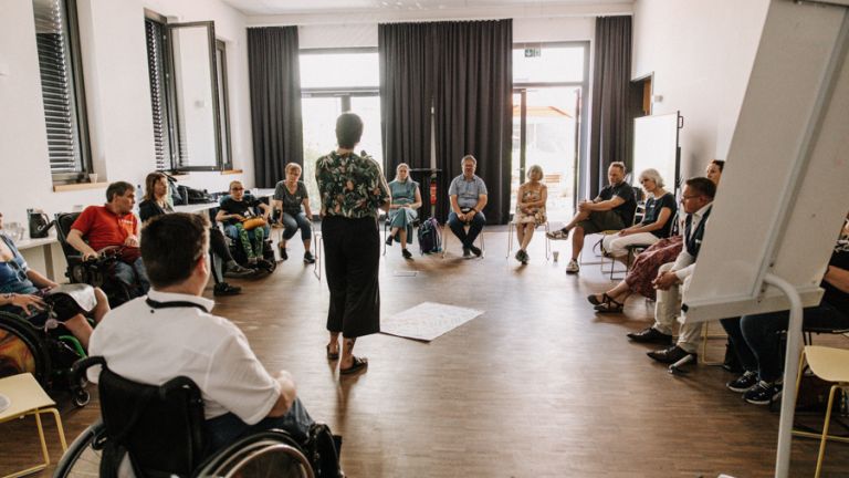 Foto eines EUTB-Netzwerktreffens. Eine Gruppe von Menschen sitzt im Stuhlkreis. In der Mitte des Kreises liegen mehrere Flipcharts mit Notizen auf dem Boden.